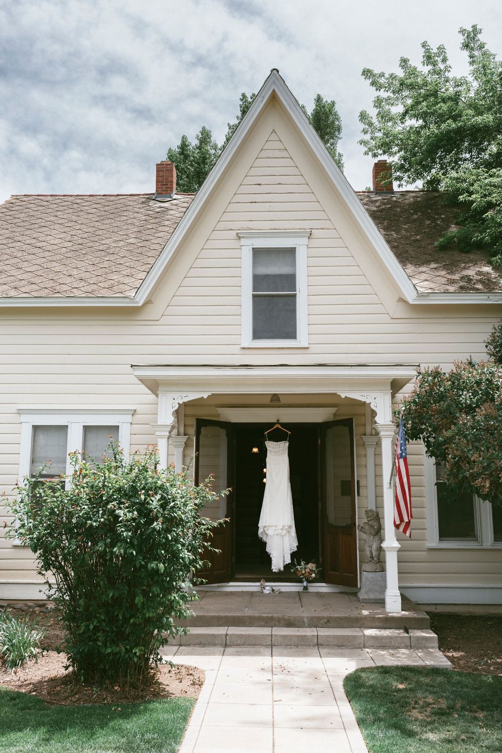 A white wedding dress hangs from the open doorway of a charming cream-colored Victorian style house with a pointed roof in Gardnerville, NV