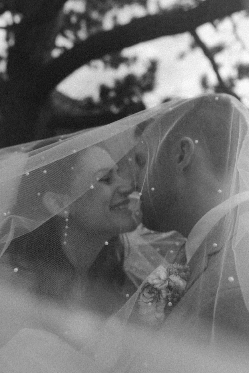 A romantic black and white portrait of a couple sharing an intimate moment under a delicate wedding veil at lake tahoe