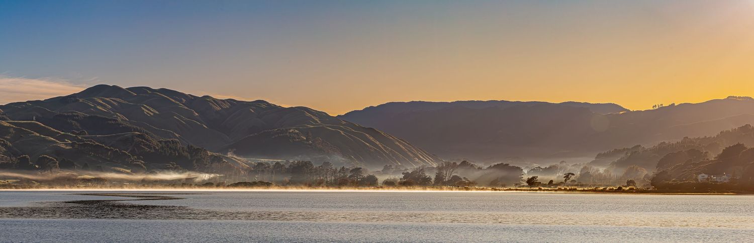 Sunset view of mountains and hills surrounding a calm inlet with misty valleys.