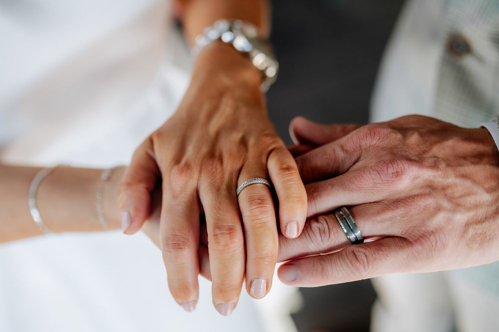 Close-up of two hands wearing wedding rings, gently touching, symbolizing love and commitment.