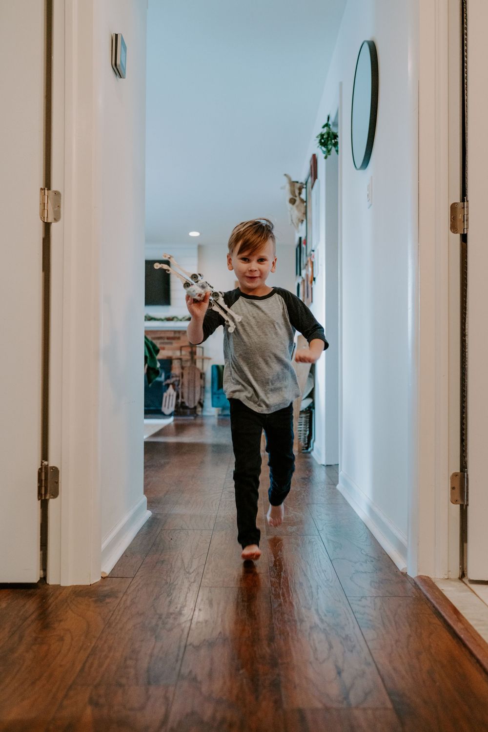 Playful family photography of a young child running down hallway of their home with his toy lego creation.