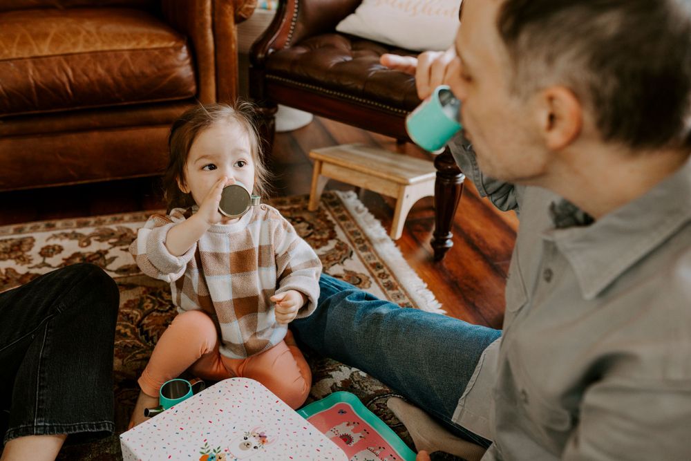 Playful family photography showing a dad playing tea party with his young daughter in their home.