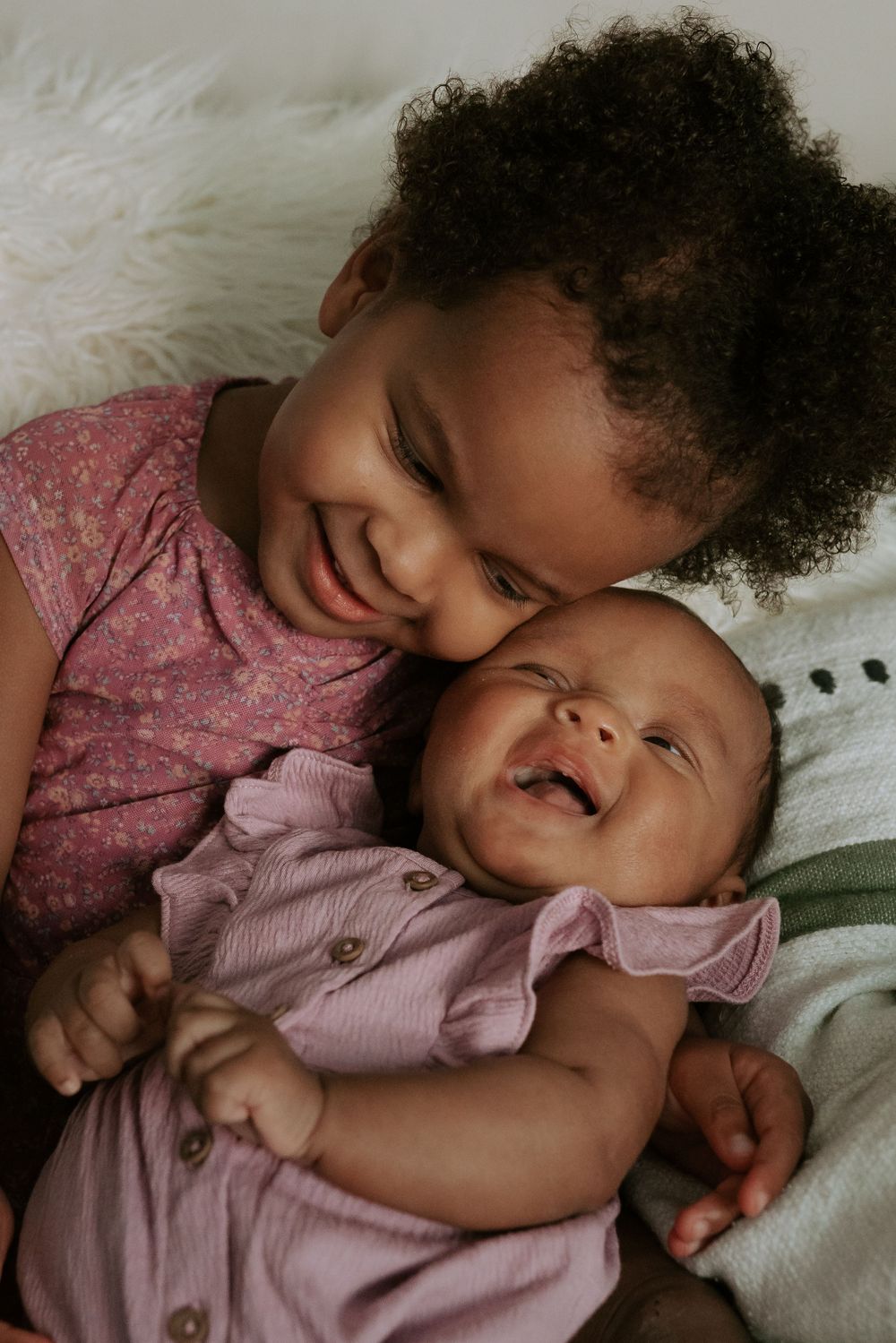 Sentimental family photography of two sisters snuggling with genuine smiles and laughter.