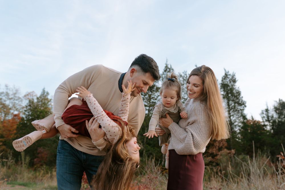 Family photography of family of four in beautiful outdoor field holding up their children in the air.