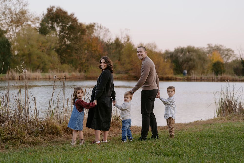 A family enjoying a peaceful autumn evening by a lake with fall foliage in the background.