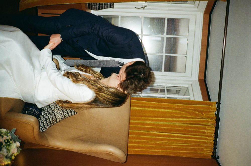 Person lying across a light brown wooden chest near a window in what appears to be a bedroom.