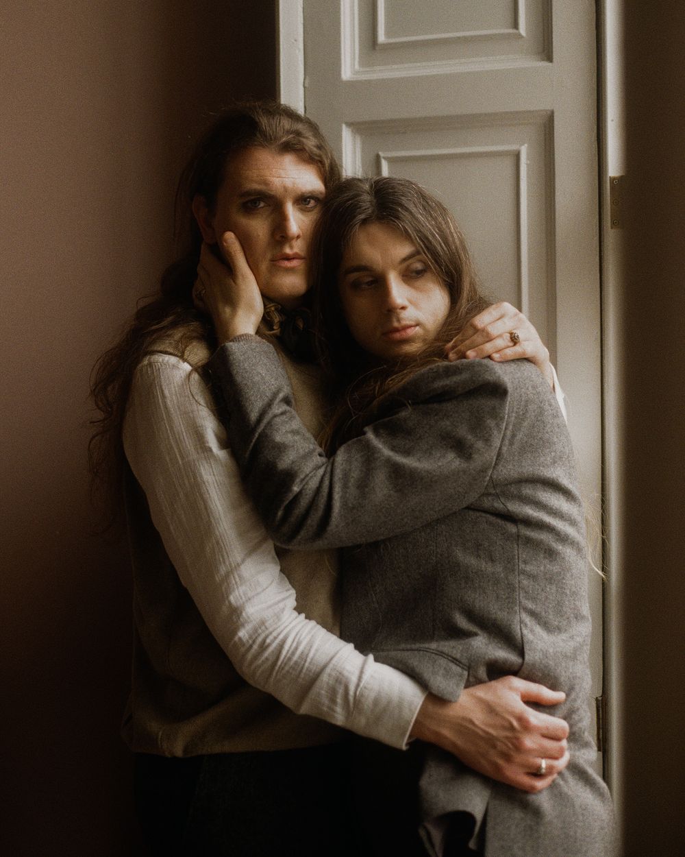A moody and intimate series of monochrome portraits showing two figures embracing against a white wall in low light.