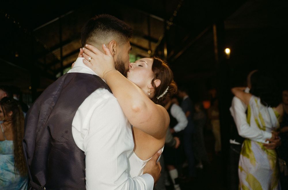 A couple embraces in a tender kiss during their wedding reception on a dark dance floor.