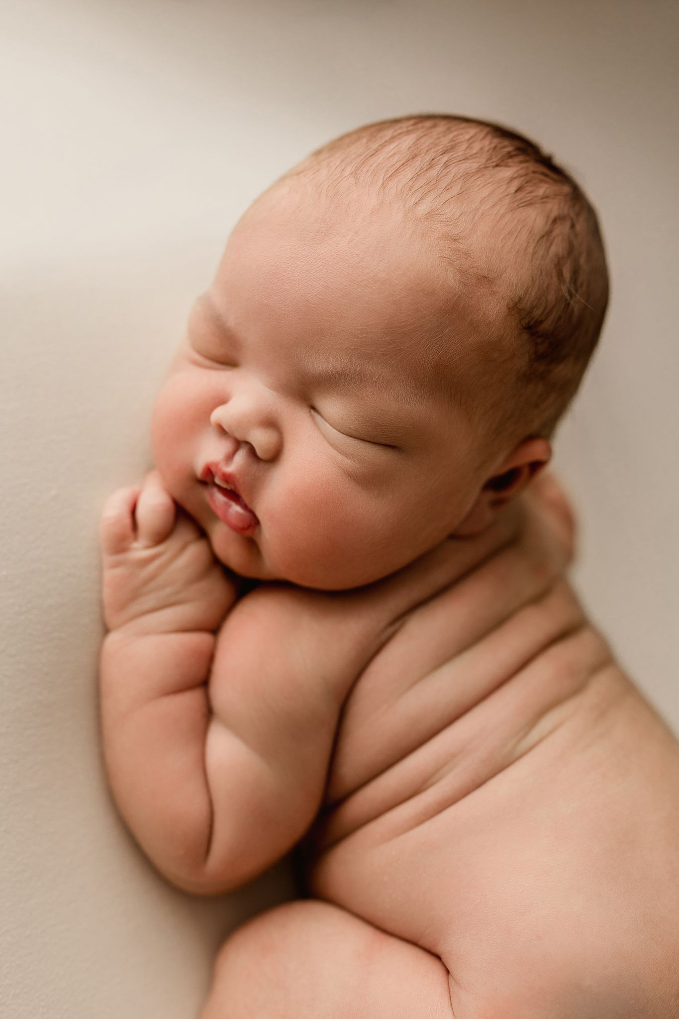 Peaceful sleeping newborn baby curled up during professional portrait session with soft beige tones.