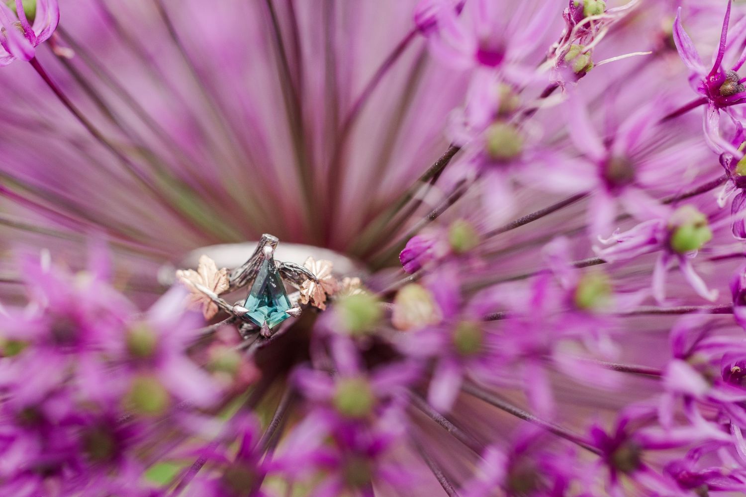 A delicate rose gold ring with teal gemstone and floral details rests on green foliage at Cantigny Park