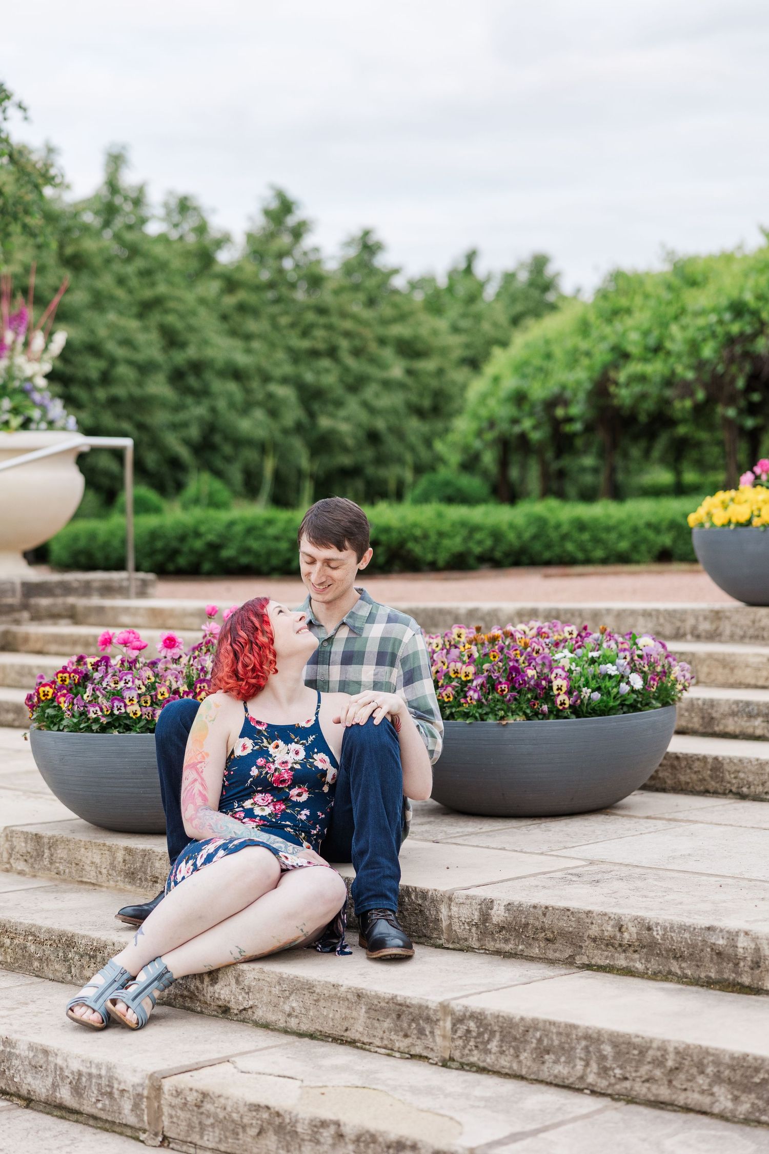 Couple sitting on outdoor stone steps with colorful flowers in planters during a romantic engagement photo session at Cantigny Park