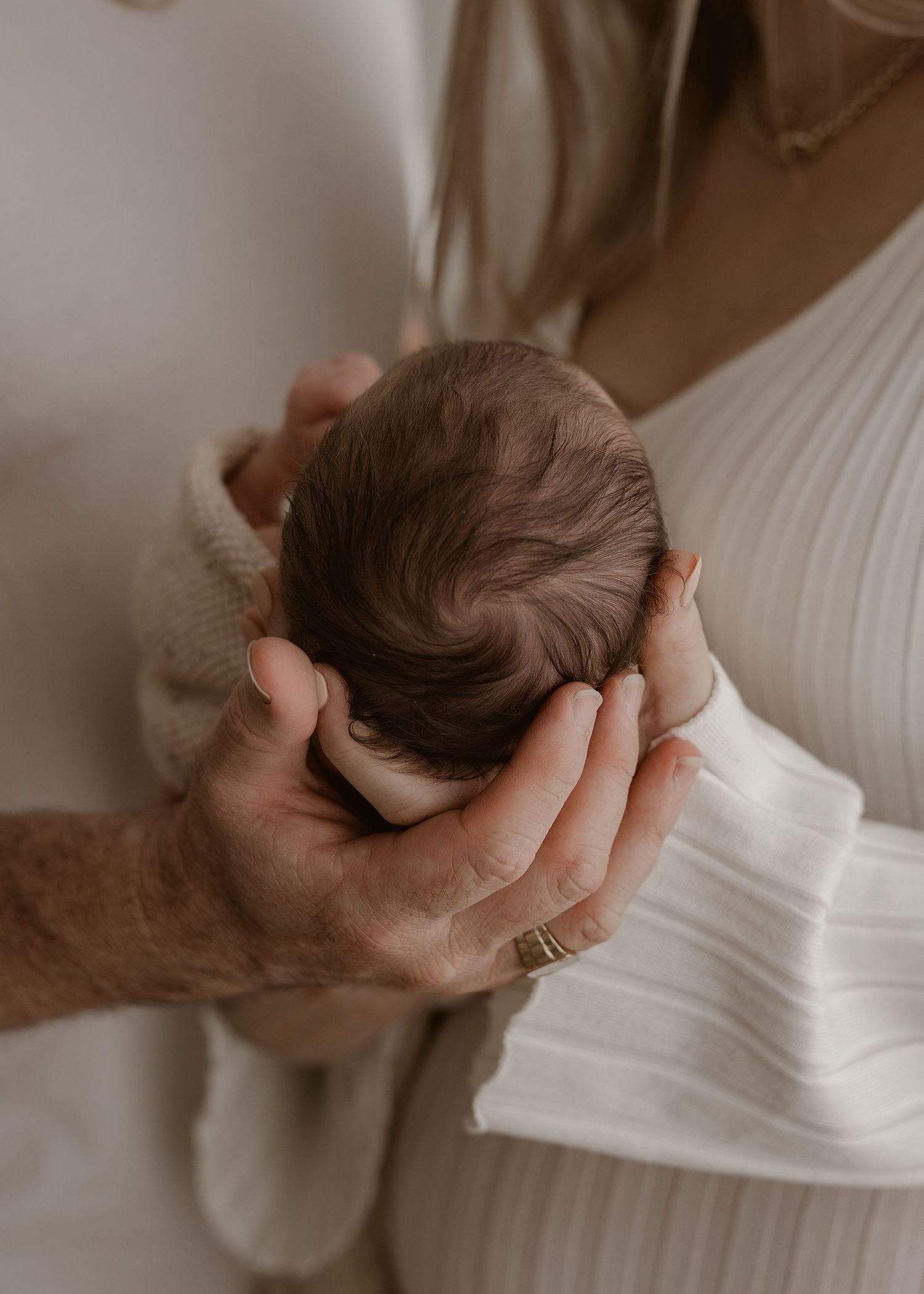 Gentle hands cradle a tiny newborn in soft, natural lighting.