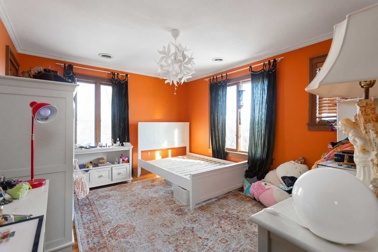 Vibrant orange bedroom with white furniture, chandelier, and patterned area rug.