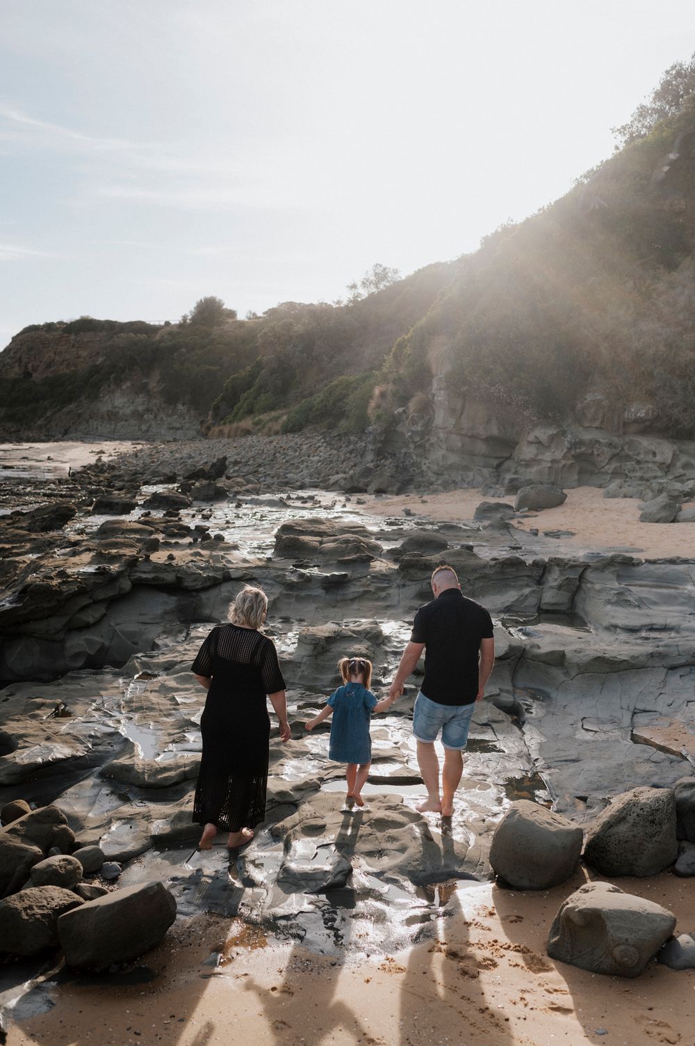 A family explores the rocky coastal landscape at sunset while walking along a sandy beach with dramatic cliffside views.