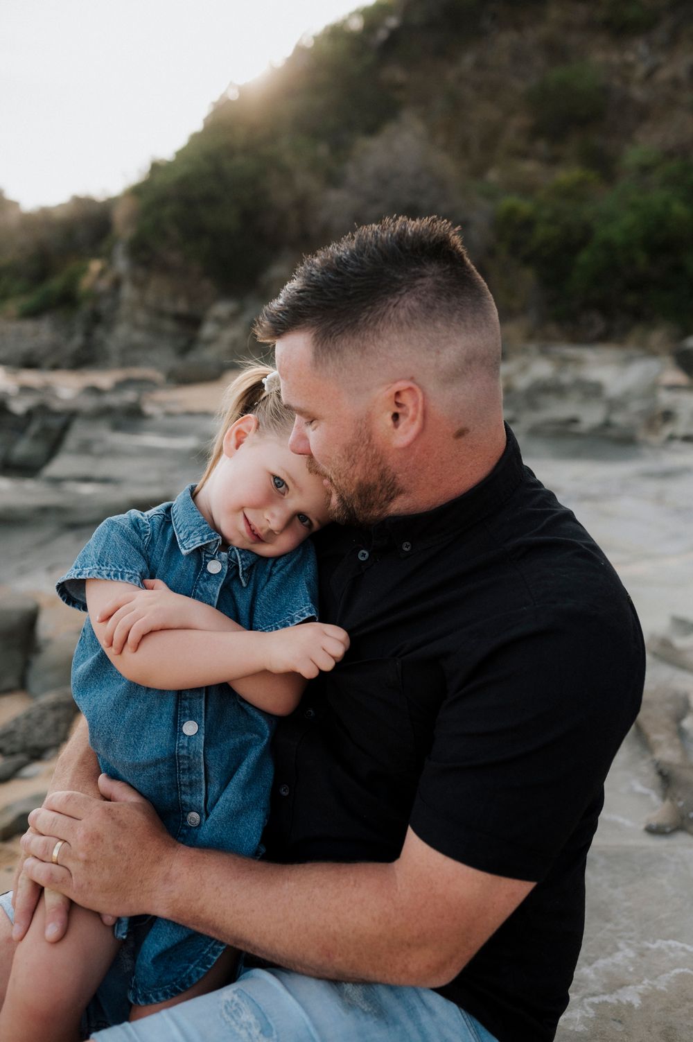 Tender moment shared between parent and child hugging on rocky beach at sunset.