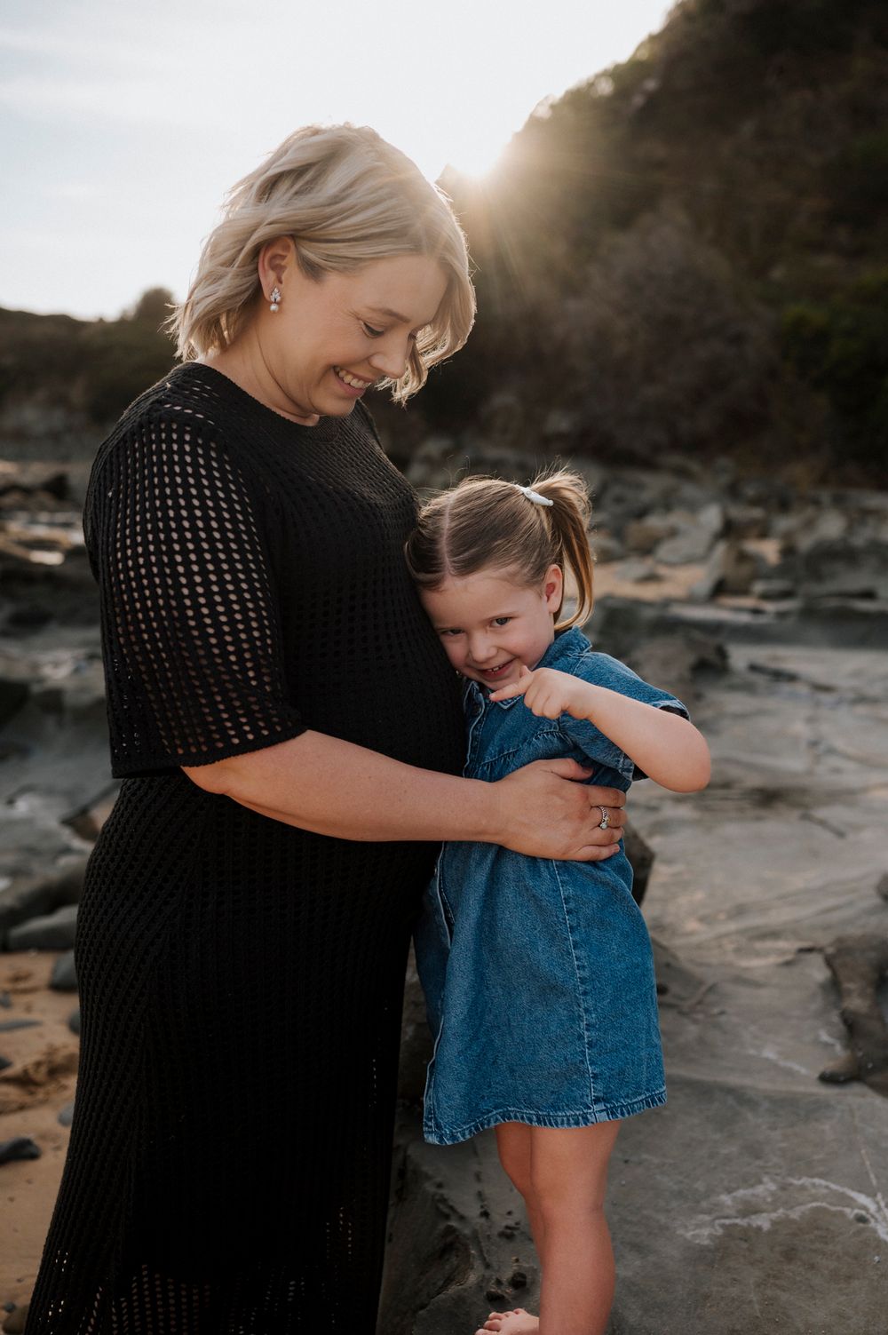 A heartfelt embrace between mother and daughter on rocky coastal shores at sunset.