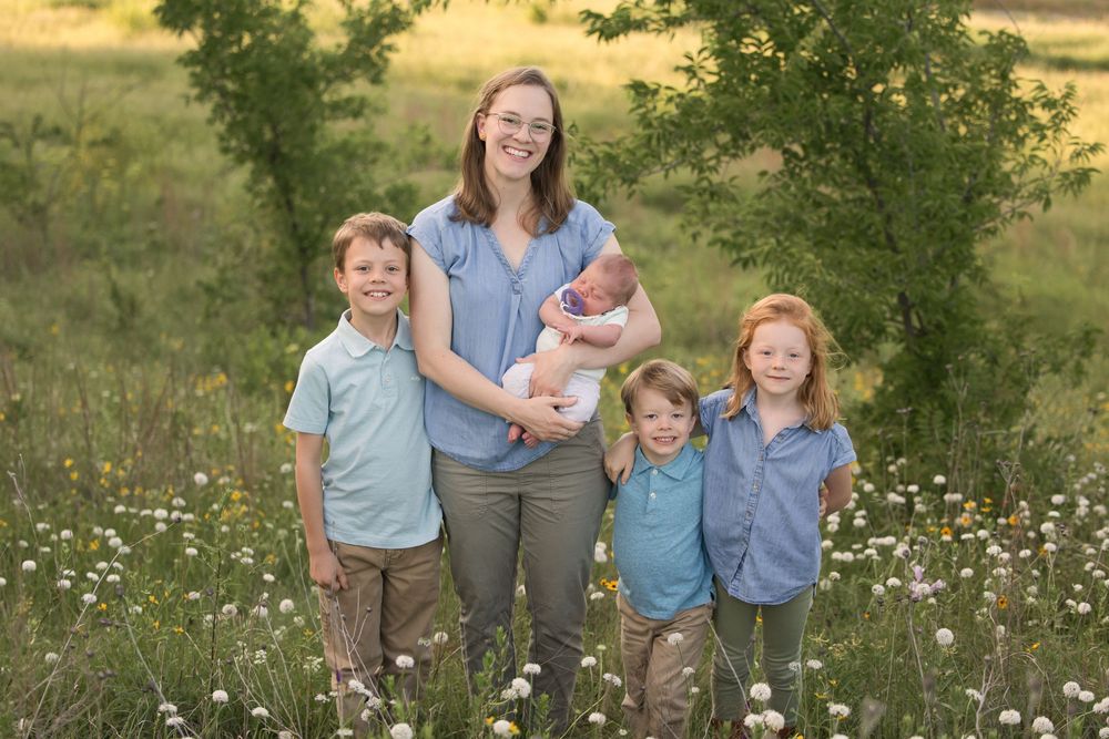 A family group stands together in a meadow filled with wildflowers during golden hour with trees in the background.