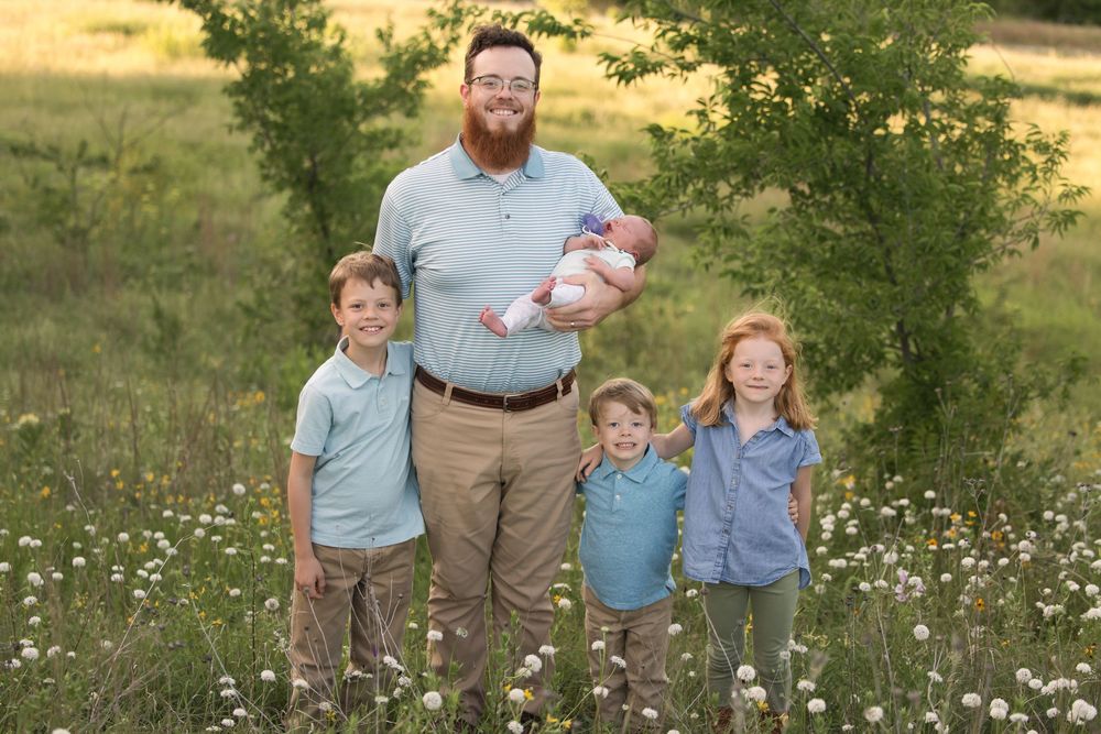 Family group poses together in a wildflower meadow at sunset wearing coordinating blue and grey outfits.