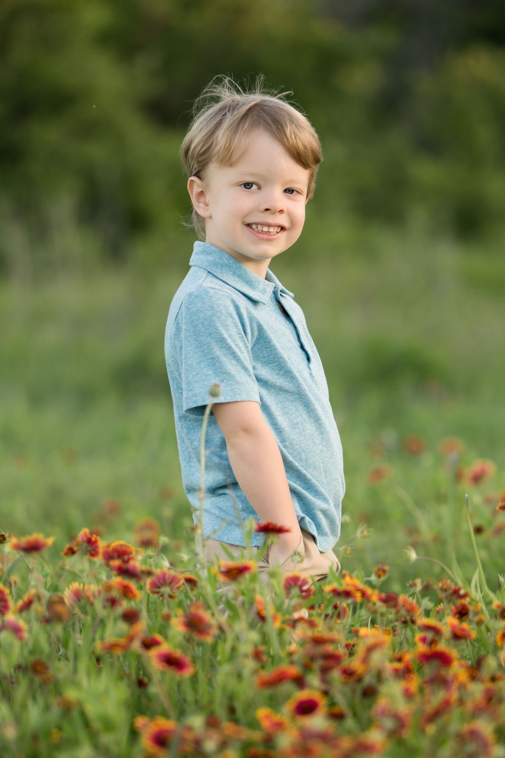 A child in a light blue polo shirt smiles while standing in a vibrant field of orange wildflowers.