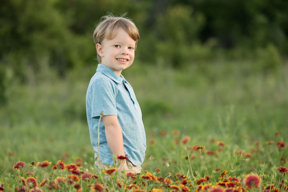 Child standing in a meadow of red wildflowers wearing a light blue shirt on a sunny summer day.