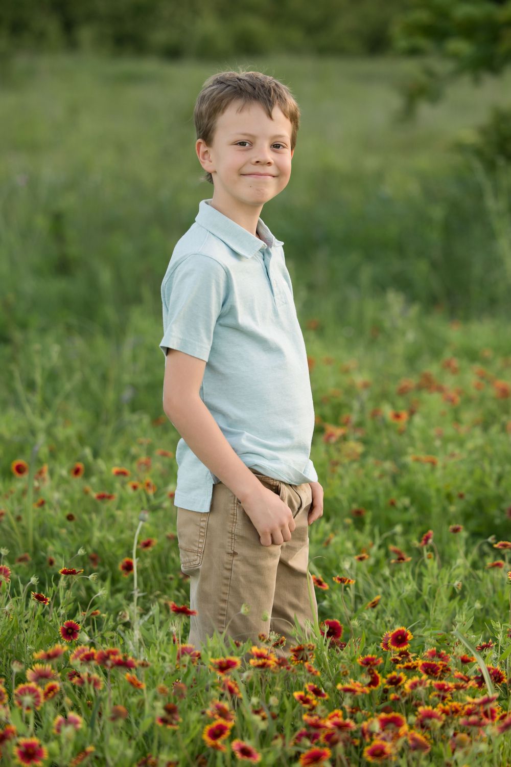A child in a light blue polo shirt and khaki shorts stands in a wildflower field blooming with red and yellow flowers.