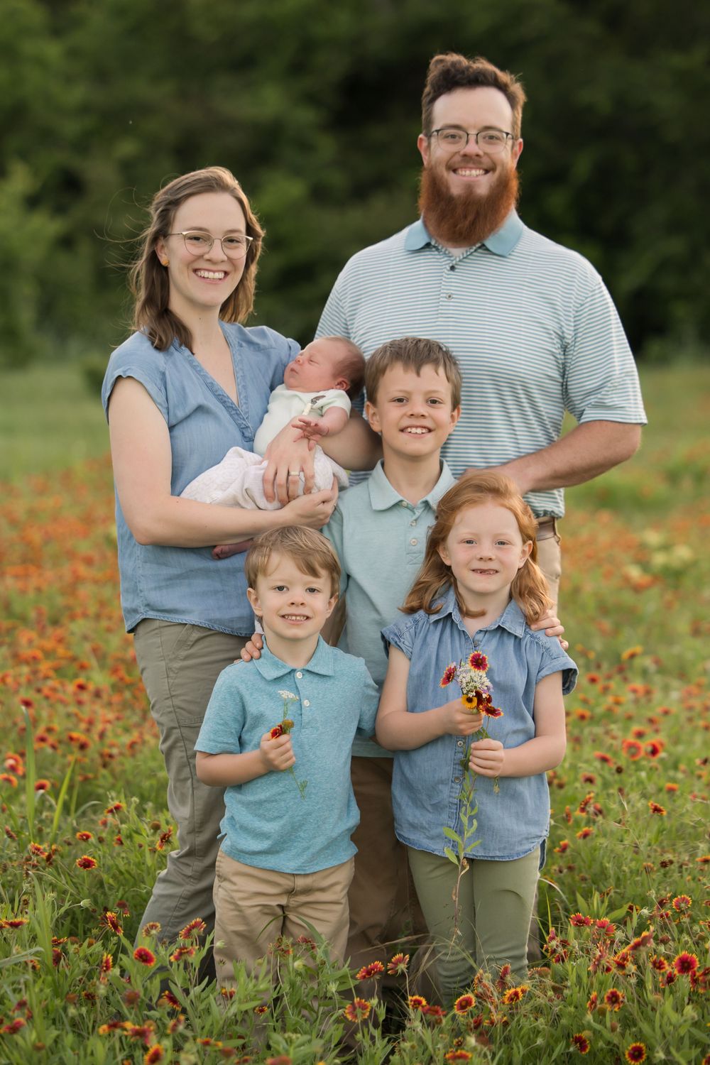 A loving family of six poses together in a vibrant wildflower field with blooming red flowers.