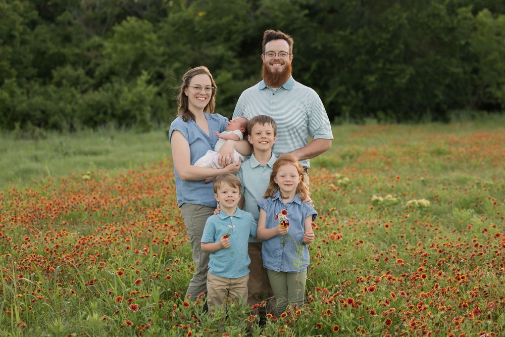 A family poses together in a vibrant field of red wildflowers on a spring day.