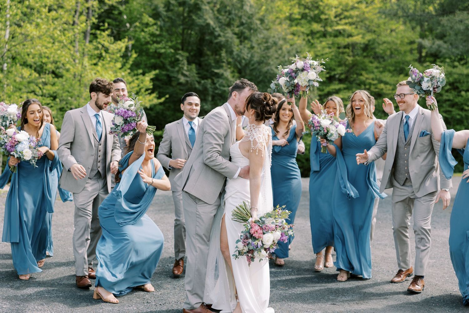 Wedding party celebrating in blue and gray attire during outdoor ceremony with bridal bouquet at Windham Manor.