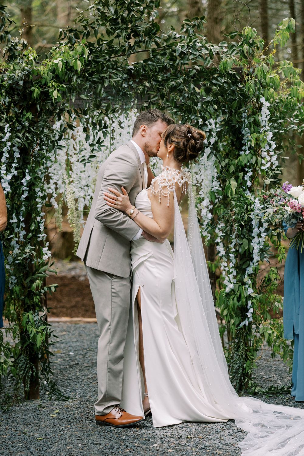 A romantic wedding couple shares a kiss under a lush floral arch decorated with cascading greenery and flowers at Windham Manor.