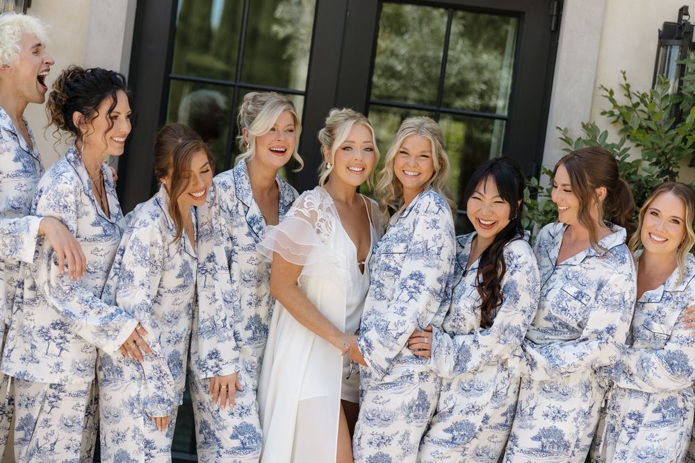 Group wearing matching blue and white patterned robes smiling together at outdoor wedding celebration.