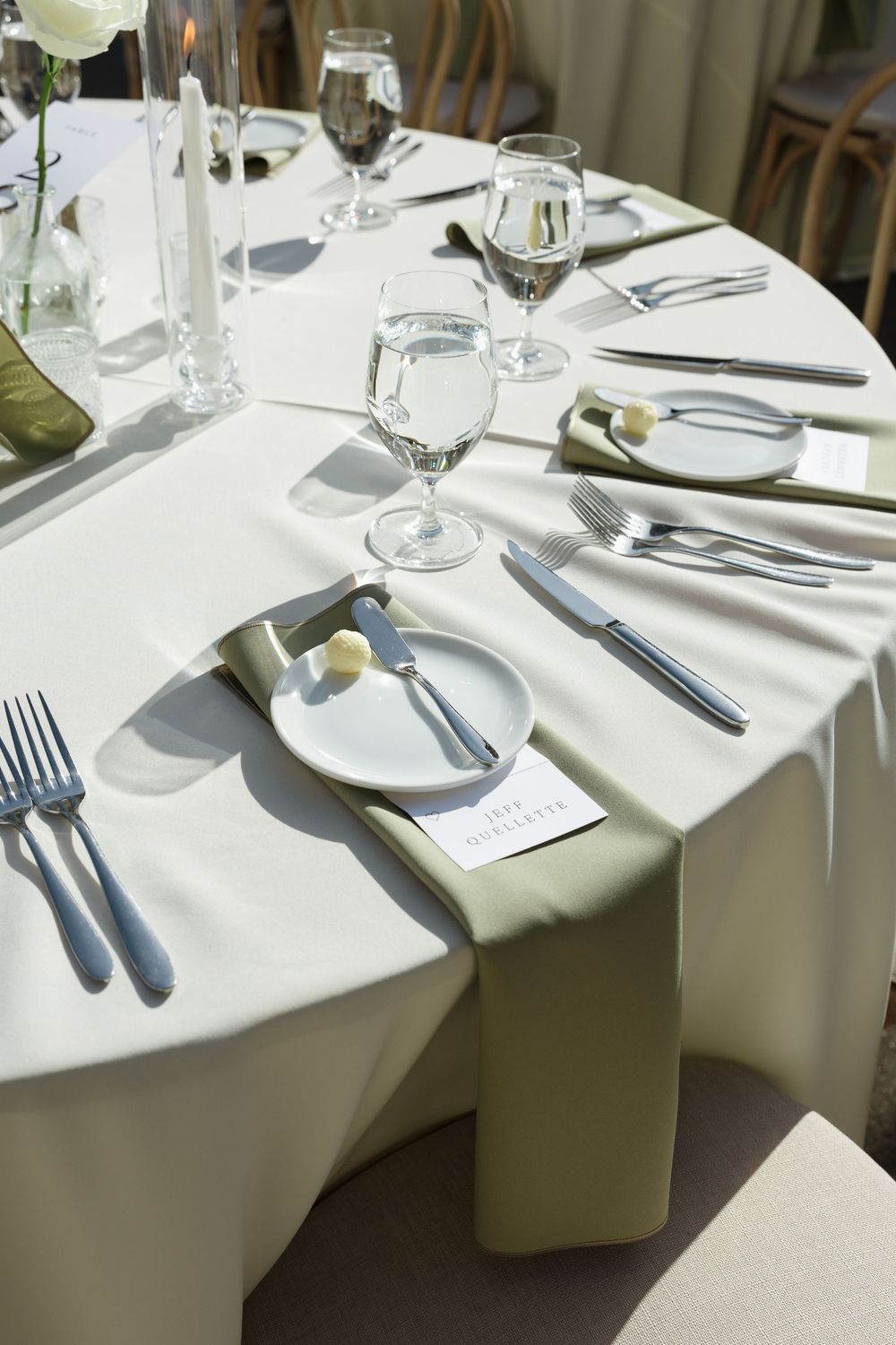 Elegant wedding table setting with white linens, wine glasses, silverware, and place cards arranged in formal dining style.