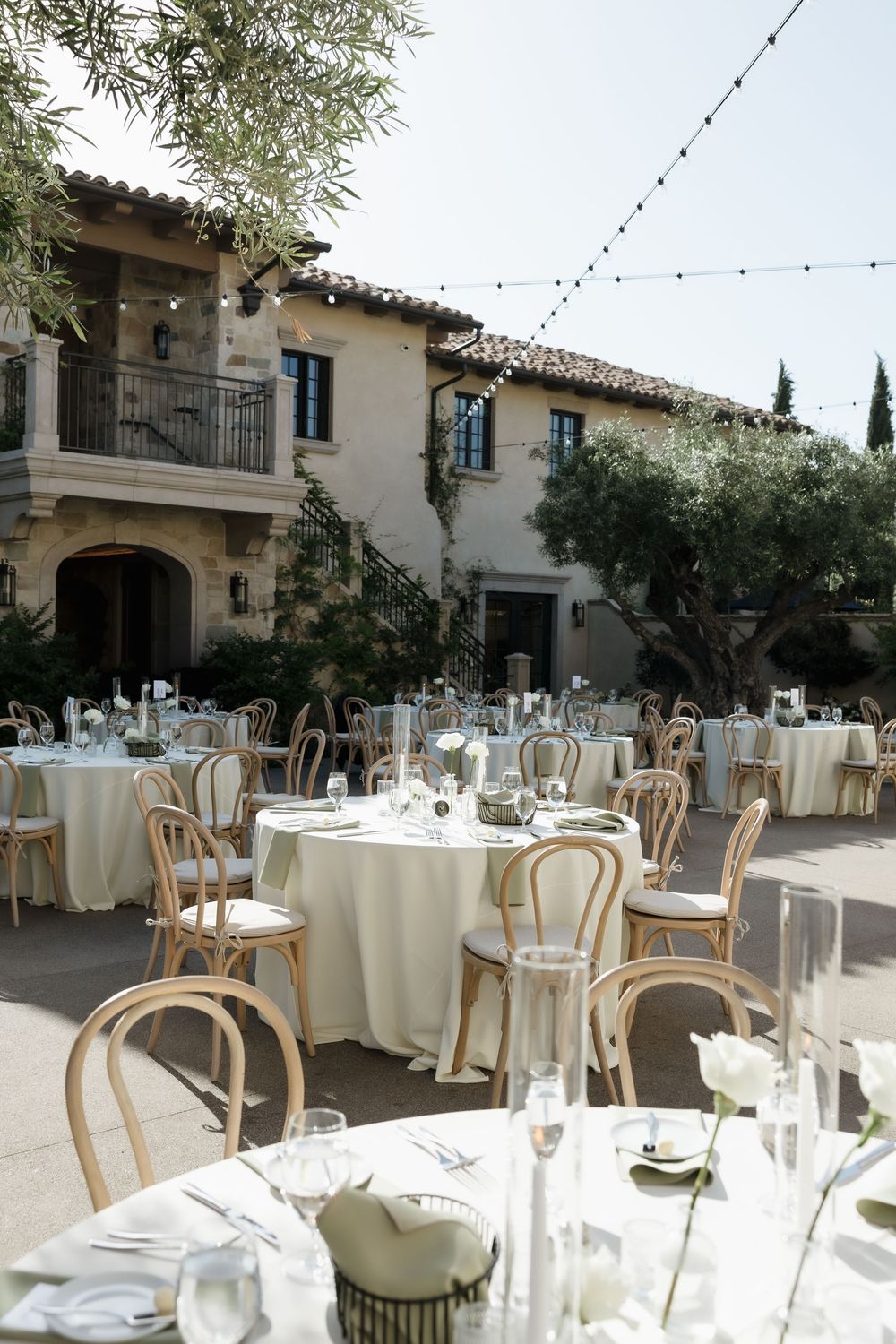 Elegant outdoor wedding reception setup with white tablecloths and bentwood chairs under string lights at a Mediterranean villa.