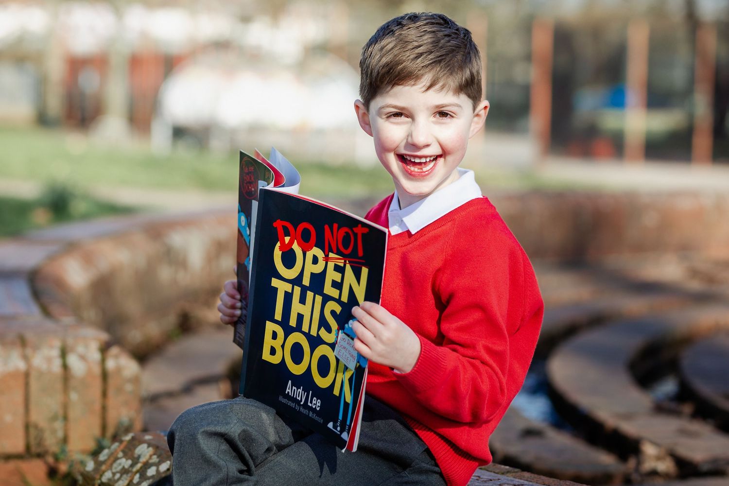 A primary school aged child reads a book & looks relaxed as he laughs to camera during school photo day. Bristol school photography