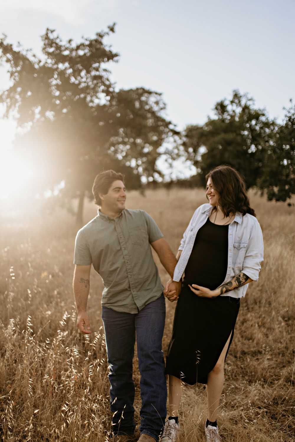 A happy couple walks together through a golden sun-lit field during a warm autumn evening maternity photoshoot in Shingle Springs.
