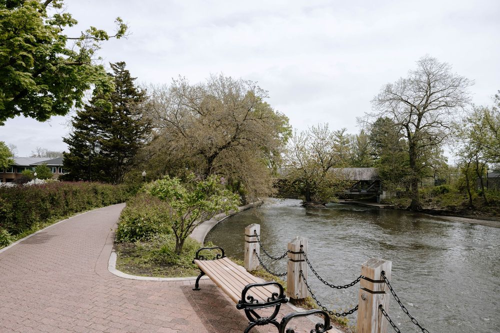 A scenic riverside walkway with wrought iron railings and a covered bridge visible in the background.