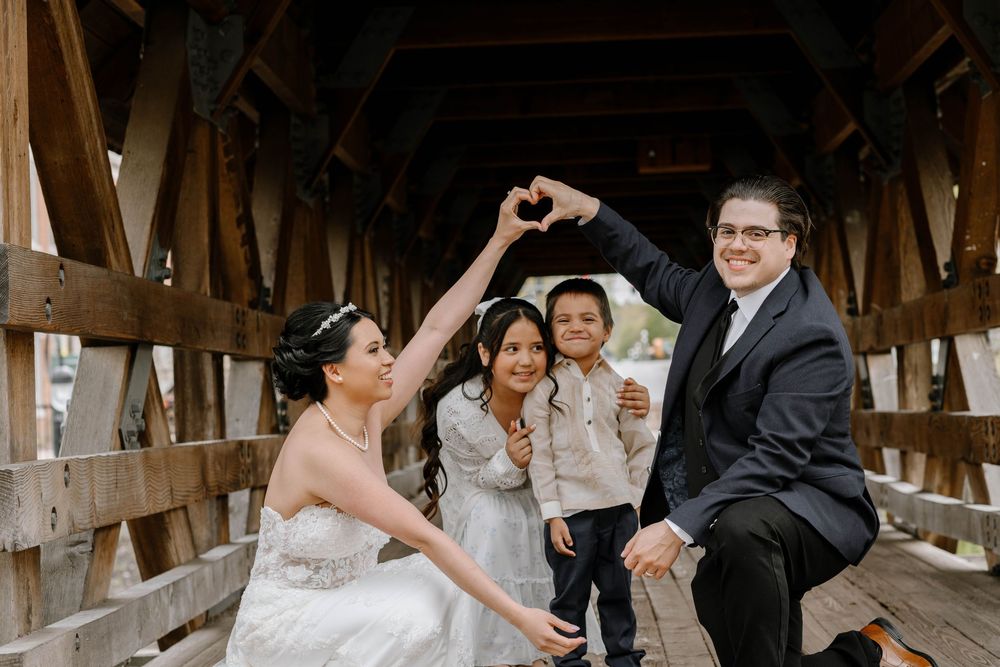 Playful wedding party poses together on a rustic wooden covered bridge.