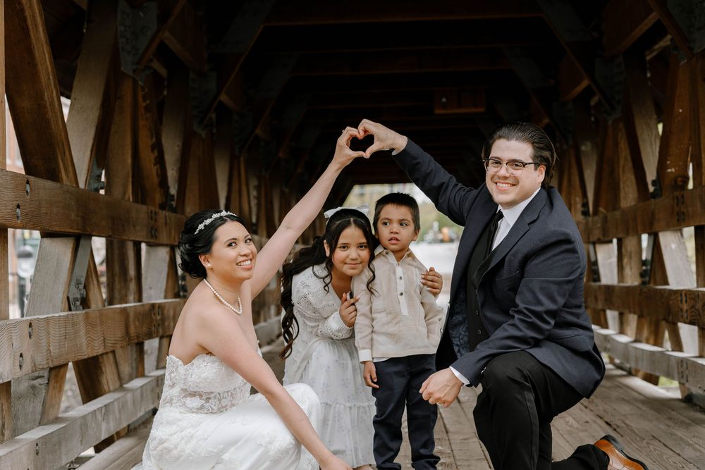 Wedding group shares a fun moment while posing on a wooden covered bridge.