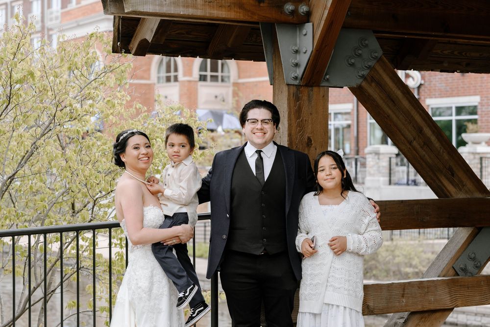 Wedding party stands together under blooming spring trees near a brick building.