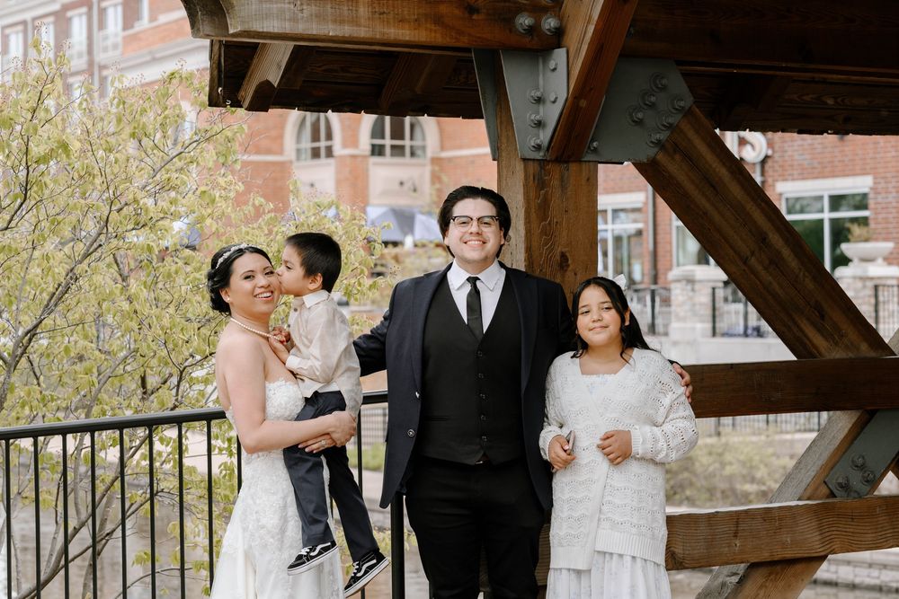 A wedding party stands beneath a wooden shelter during a spring celebration.