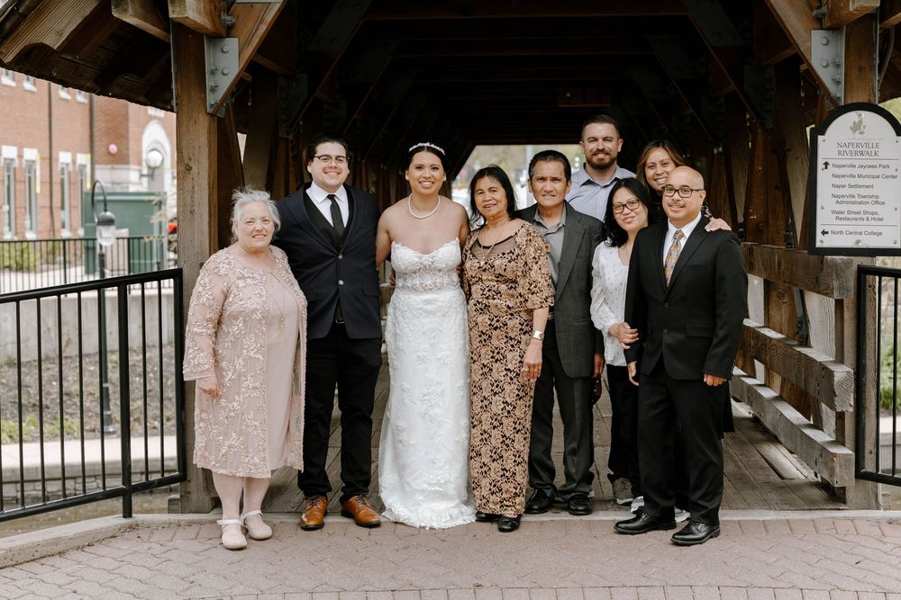 A wedding party group photo taken at the entrance of a rustic covered bridge.