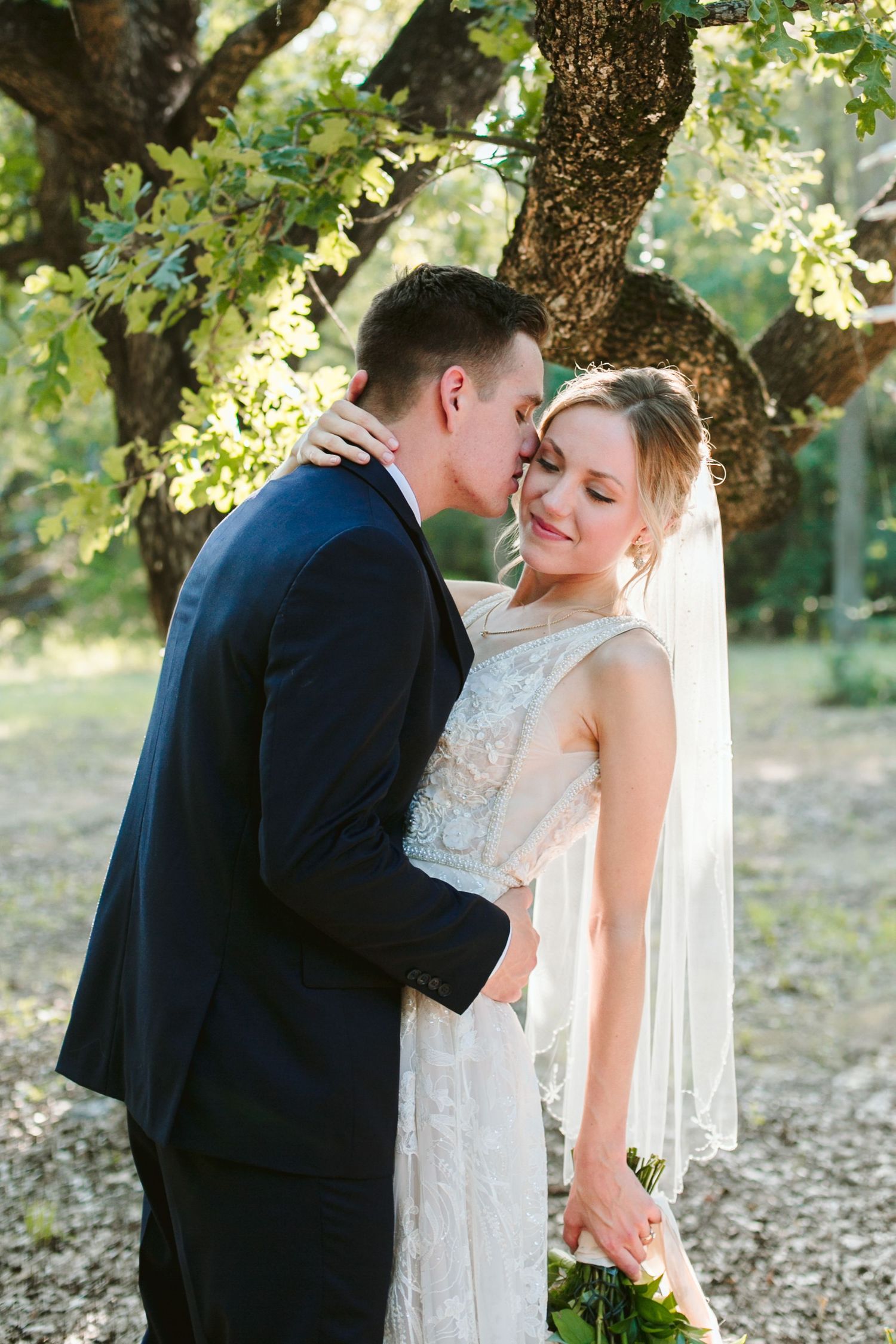 A romantic wedding moment under a branching tree with soft natural lighting.