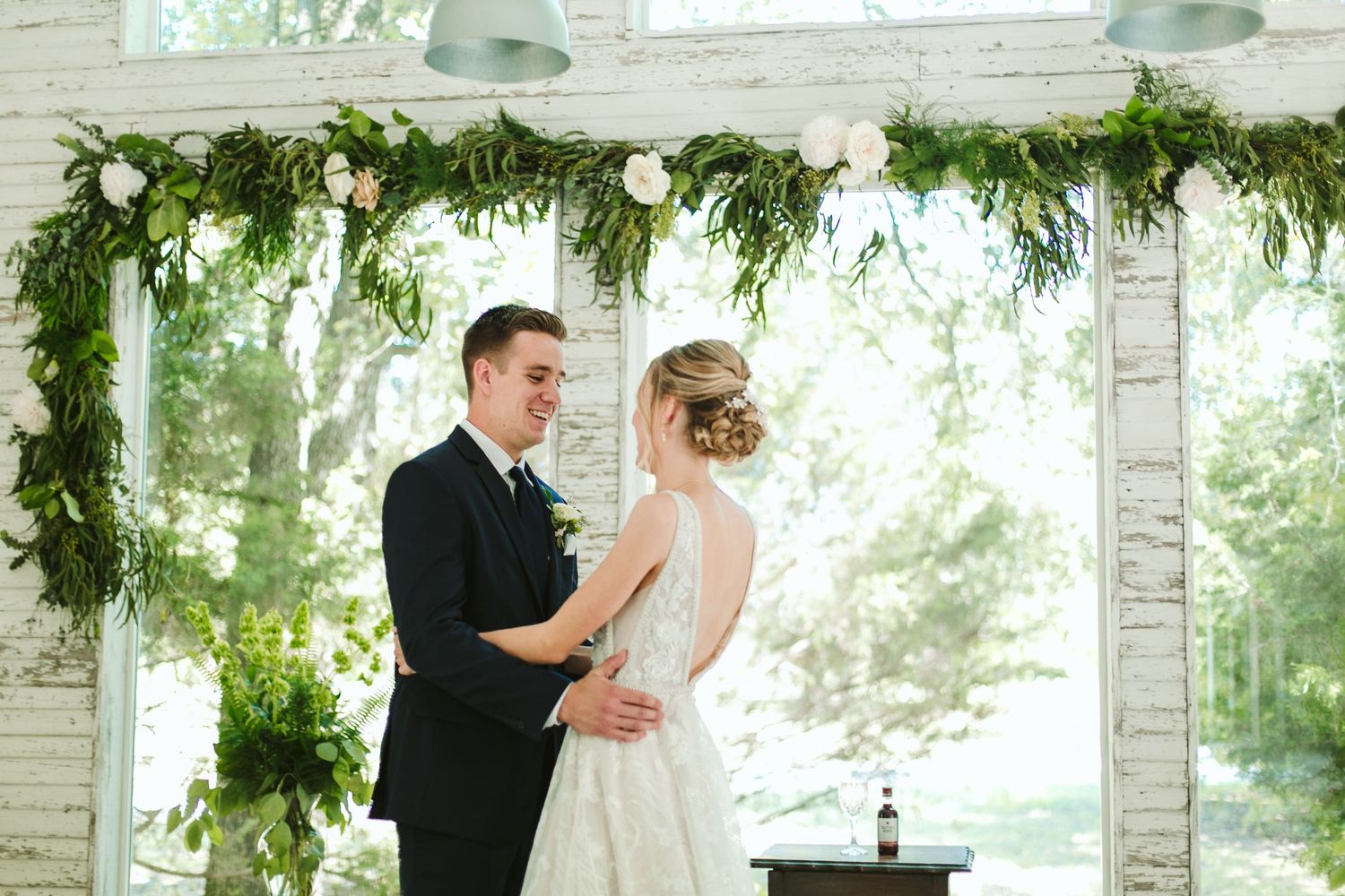 Intimate moment between newlyweds under floral ceremony arch with white accents.