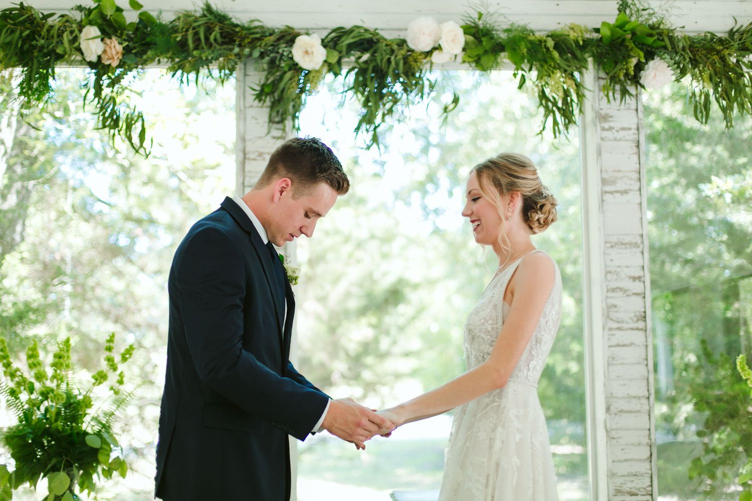 Happy couple exchanging vows under decorative greenery arch during ceremony.