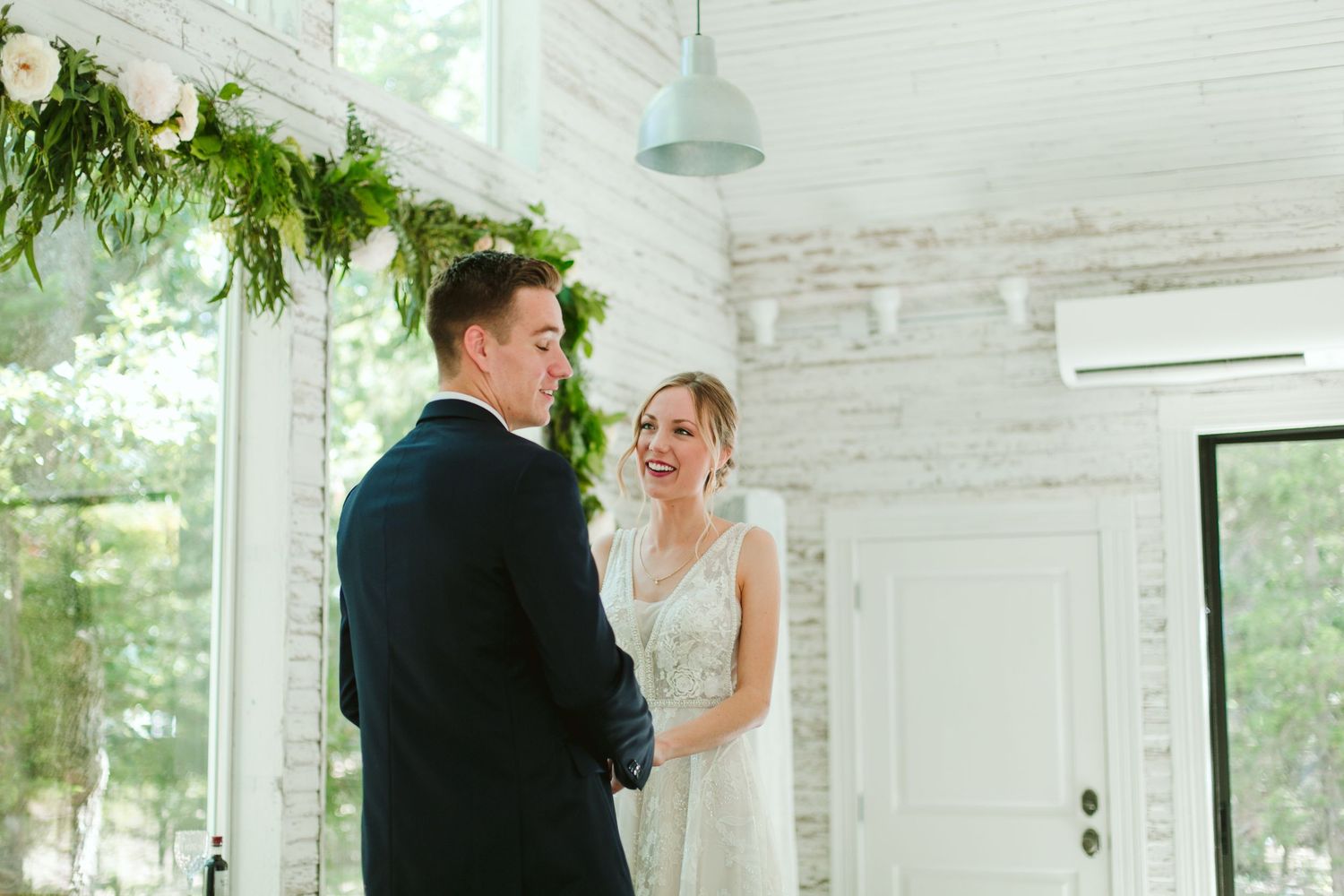Bride and groom share an intimate moment in a bright white room decorated with greenery.