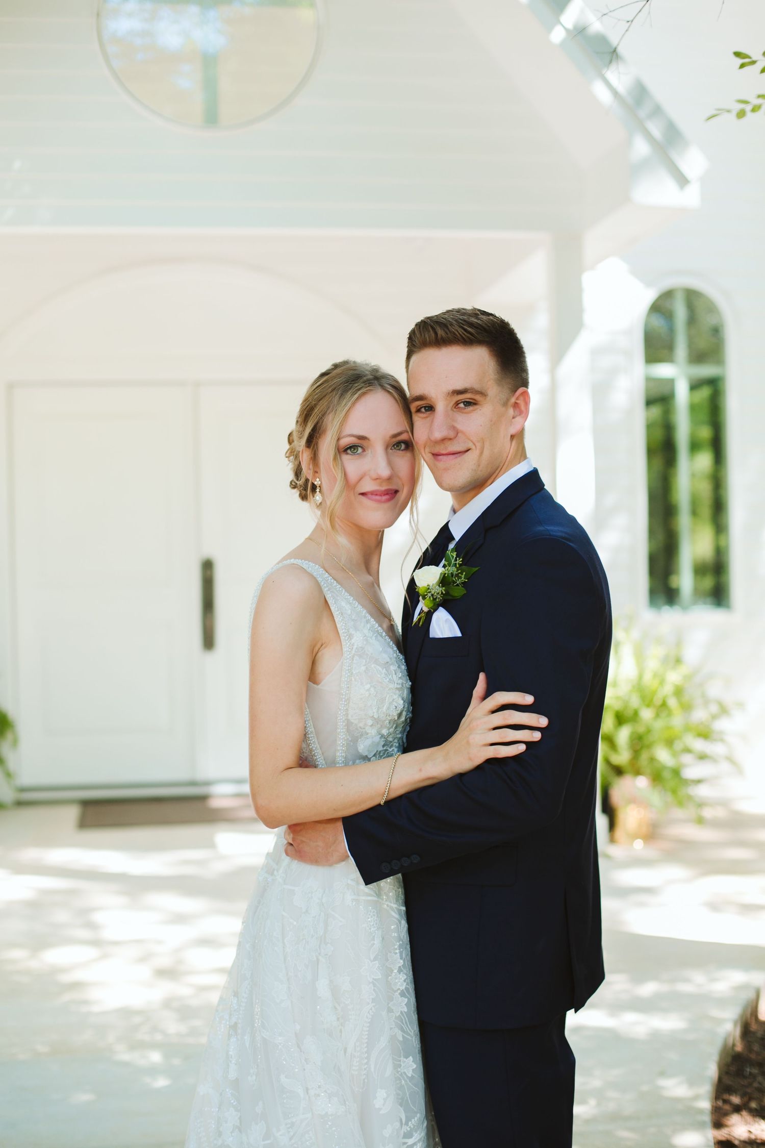 Newlyweds pose together in front of a white chapel with arched windows and natural lighting.