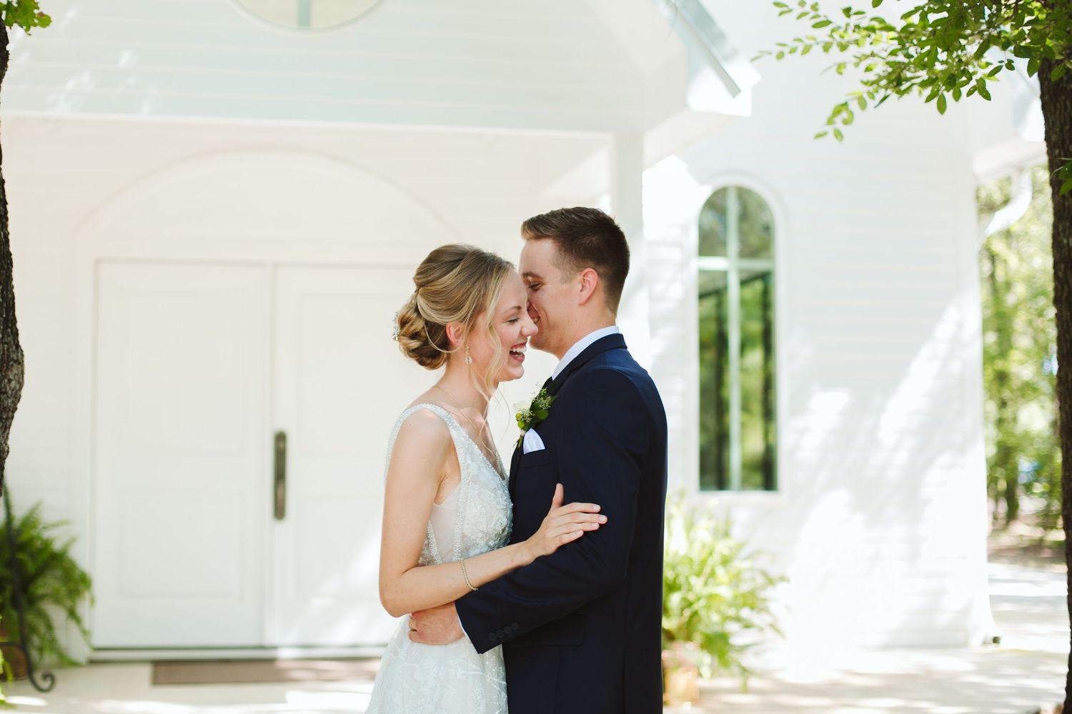 Wedding couple embraces in front of a white church entrance on their special day.