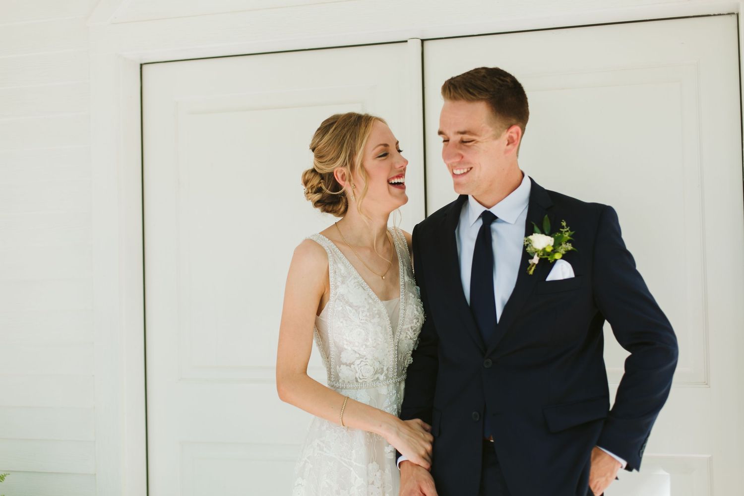 Candid moment of bride and groom laughing together against white backdrop.