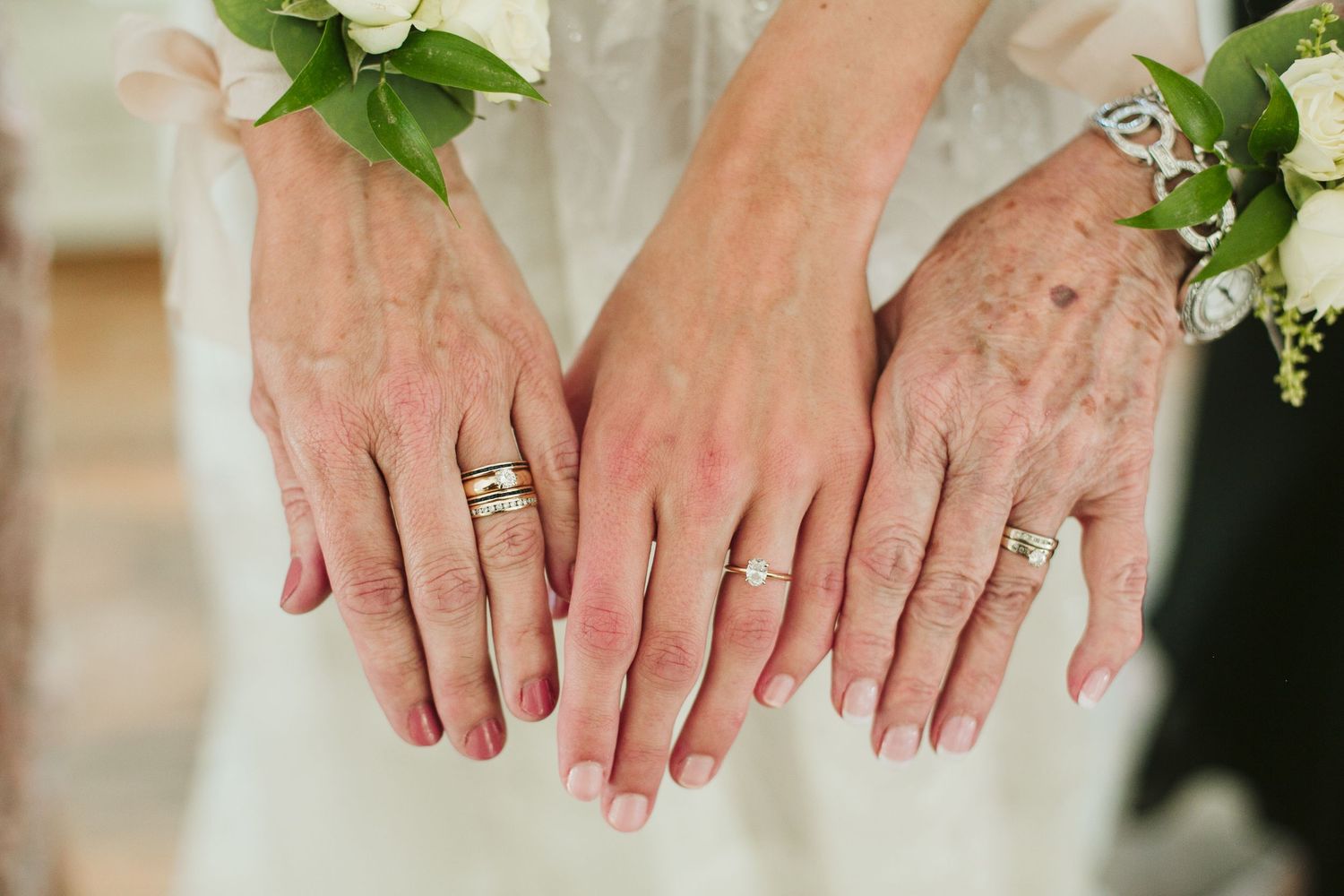 Three hands displaying wedding rings against a white floral backdrop.