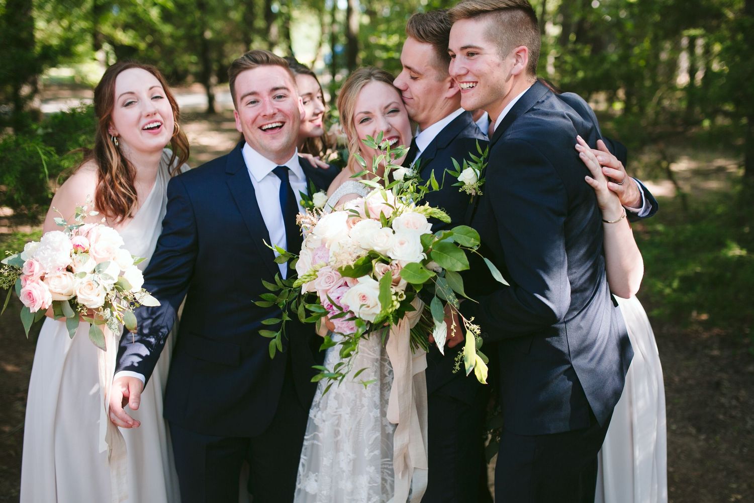 Candid moment of wedding party laughing together in forest setting.