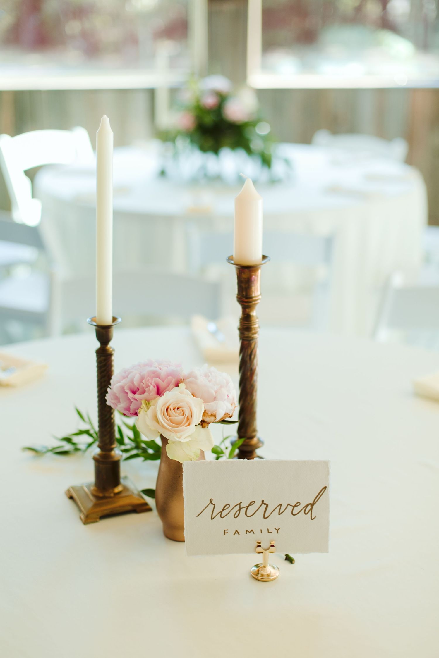 Elegant table setting with white taper candles, pink roses and reserved sign for family.